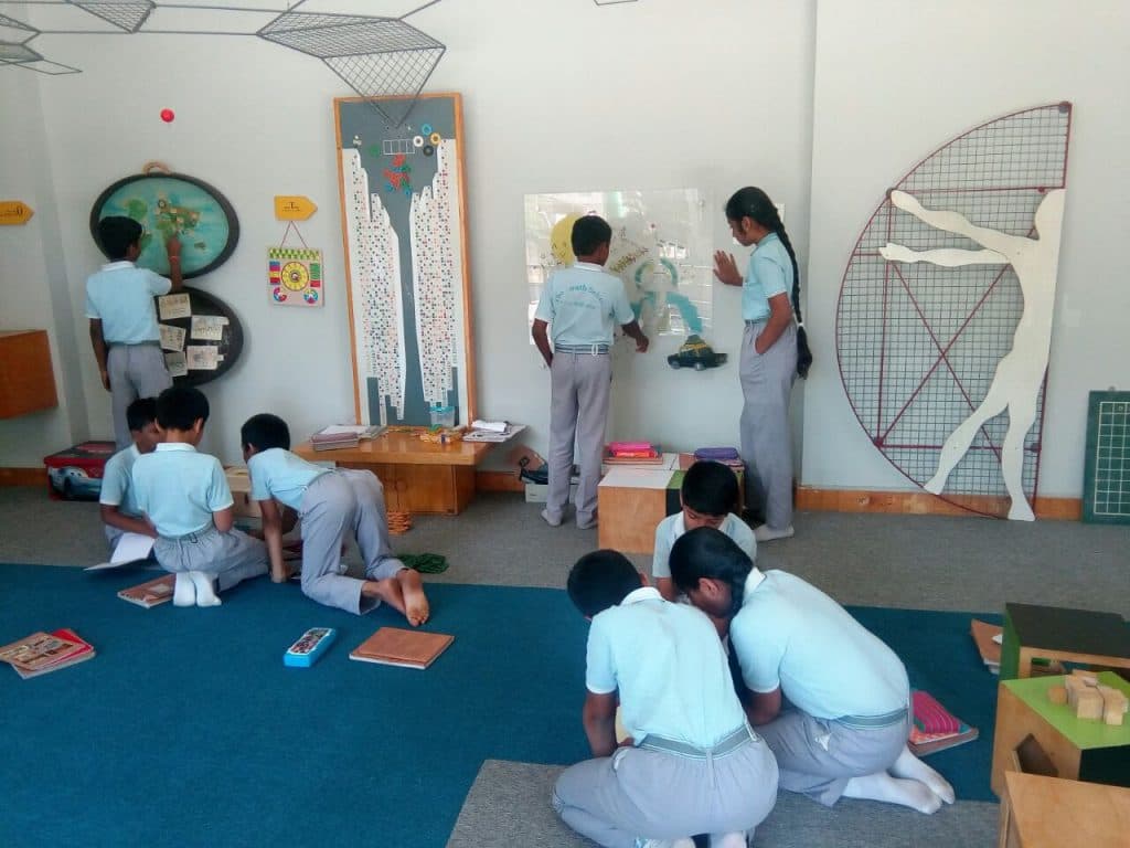 Primary school children working on the floor with charts, cards and wooden learning materials